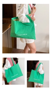 Detail of green nylon tote bag featuring white letter printing and wide shoulder straps