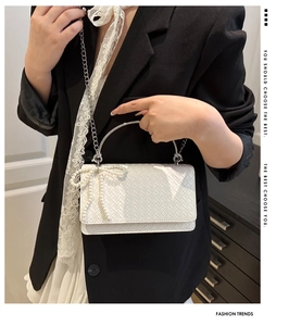 Detail of white woven handbag featuring pearl bow decoration and silver metal handle
