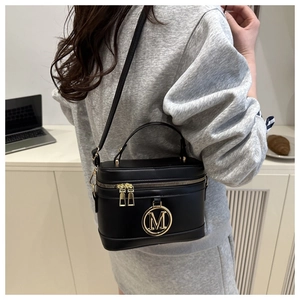Side view of model wearing a black box-style crossbody bag with gold M metal logo
