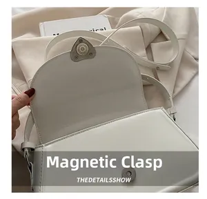Detail view of the heart-shaped magnetic buckle on a white leather rectangular crossbody bag