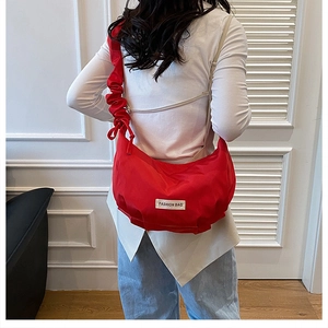 Detail of red nylon crescent bag featuring pleated shoulder strap and brand logo label
