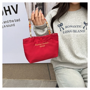 Detail of red tote bag featuring colorful braided handles and elegant letter embroidery