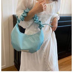 Macro detail of a light blue nylon dumpling bag with pleated handle and fashion label