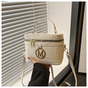 Detail of white box bag featuring a gold metal M logo and smooth leather texture