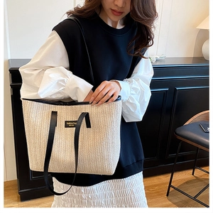 Close-up of beige straw tote bag featuring a V-shaped weave and black leather handles