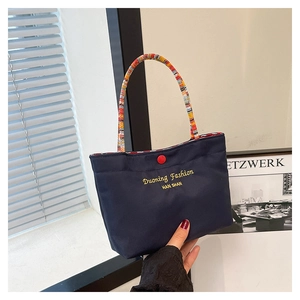 Detail of navy canvas tote bag featuring red button and colorful woven handles