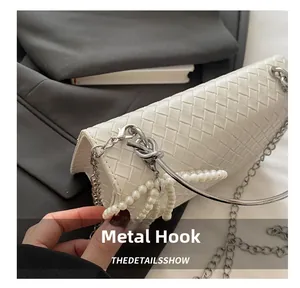 Detail of silver hardware hook and pearl tassel on white woven crossbody bag