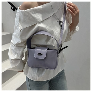 Nahaufnahme der fliederfarbenen Lacktasche mit Metallemblem und abnehmbarem Gurt