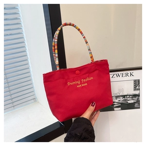 Detail of red fabric handbag featuring a colorful woven handle and golden lettering