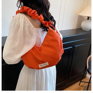 Detail of a bright orange nylon dumpling bag featuring a ruffled shoulder strap and logo
