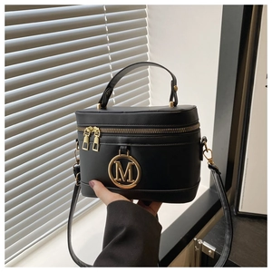 Close-up of black box bag showing gold M logo and elegant leather texture on hand