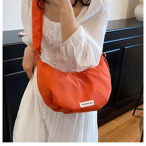 Detail of orange nylon dumpling bag featuring wide shoulder strap and fashion label