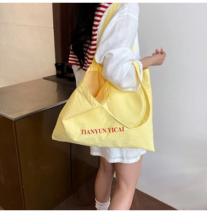 Detail view of large yellow canvas tote bag with red letter print worn on the shoulder