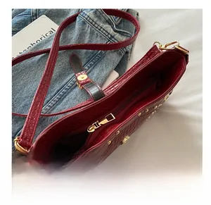 Detail of burgundy crocodile pattern handbag showing smooth gold zipper and rivet accents