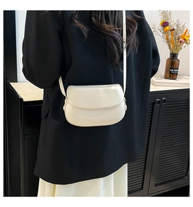 Close-up of a minimalist white saddle bag showing smooth leather texture on a model