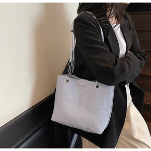 Detail of light gray textured tote bag with metal chain strap on a model shoulder