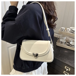 Detail of minimalist cream shoulder bag featuring a silver heart-shaped magnetic buckle