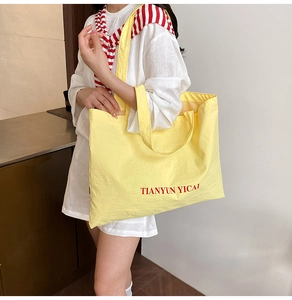 Detail of yellow canvas tote bag with red lettering on a model for lifestyle view