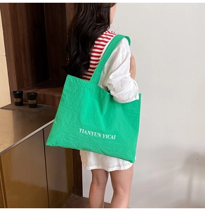 Detail showing the large green canvas tote bag with white art font lettering print