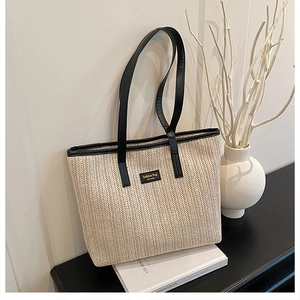 Close-up of woven straw tote bag featuring contrast black leather trim and logo patch