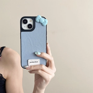 Sky blue leather phone case with a 3D bow and branded label held by a hand