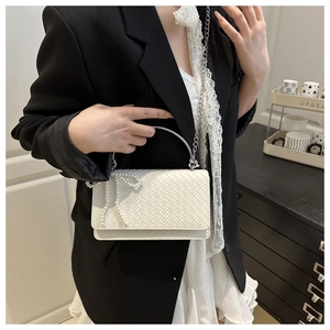 Detail of white woven leather handbag with silver arch handle and pearl bow charm