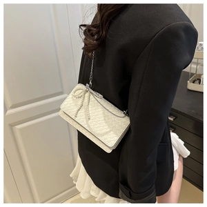 Detailed side view of white woven shoulder bag with pearl bow and silver chain