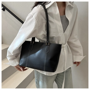Detail of black leather tote bag with white contrast stitching and gold metal hardware