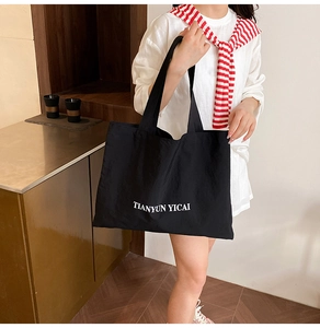 Detail of large black canvas tote bag with white TIANYUN YICAI print and long shoulder straps