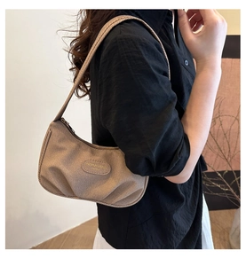 Dettaglio di una borsa sottobraccio marrone a pieghe indossata da una modella in nero.