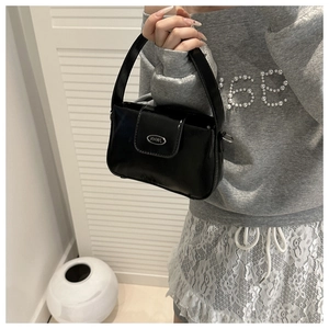 Detail einer glänzenden schwarzen Ledertasche mit silbernem Metalllogo und Tragegriff