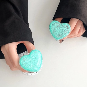 Detail of heart-shaped mint green glitter phone grip with star design held by hands