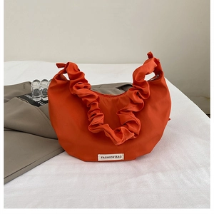Detail of bright orange nylon dumpling bag with ruffle shoulder strap and fashion label