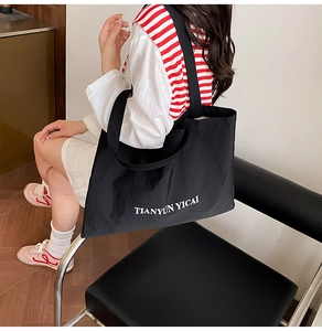 Detail of black large capacity tote bag with white letter print and wide shoulder strap