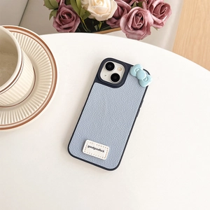 Close-up of light blue leather phone case with 3D bow and Goodluck label on a table