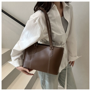 Detail of dark brown leather tote bag with contrasting white stitching and slim straps
