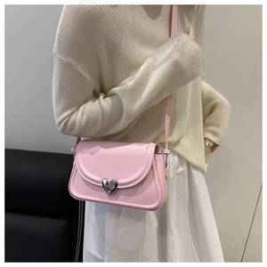 Detail of pink leather crossbody bag with silver heart buckle on model beige outfit