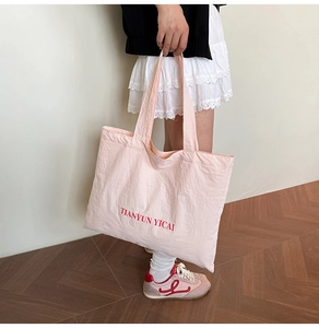 Detail of a pink tote bag with red embroidered text showing high-capacity texture