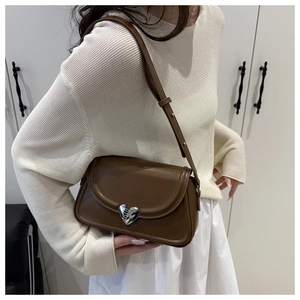Detail of a dark brown crossbody bag featuring a unique silver heart-shaped metal buckle