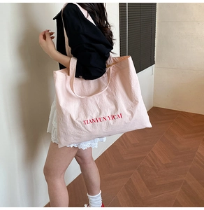 Close-up of pink canvas tote bag with red letter print worn over a casual outfit
