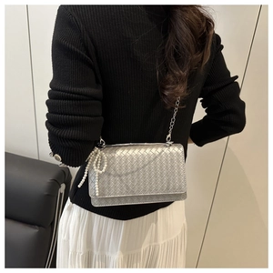 Silver woven crossbody bag detail with pearl bow charm on model wearing white skirt