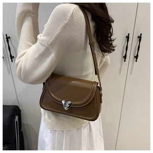 Detail of caramel leather shoulder bag with silver heart buckle worn by model