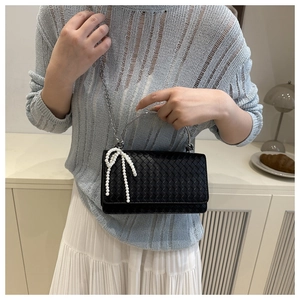 Detail of black woven texture bag with silver handle and elegant pearl bow charm