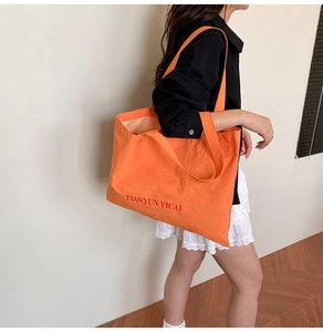 Close-up of bright orange canvas tote bag with red lettering on a model shoulder