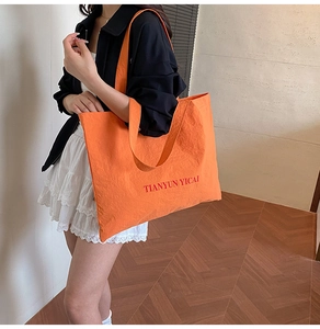 Detail of orange tote bag featuring unique crinkled texture and bold red lettering print