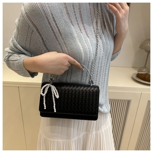 Detail of woven leather shoulder bag with pearl bow charm and metal handle shown on model