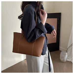 Detailed view of brown leather tote bag showing white contrast stitching and hardware