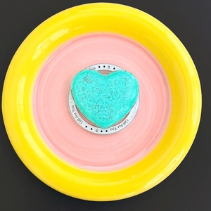 Top view of a bright teal heart-shaped bath bomb on a Gift For You paper base