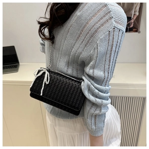 Detail of woven leather shoulder bag with white pearl bow and silver chain strap