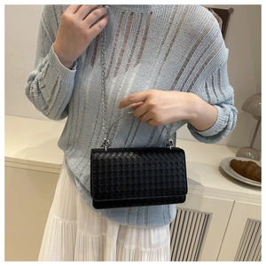 Detail of black woven leather crossbody bag with silver metal handle and chain strap